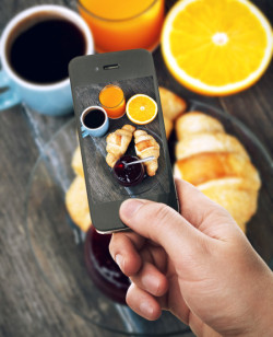 Hand with smartphone taking food photo of fresh breakfast with coffee and croissants